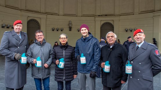 6 Personen stehen aufgereiht vor einem historischen Gebäude. Sie halten lächeln blaue Sammeldosen in die Kamera.