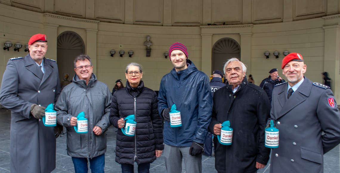 6 Personen stehen aufgereiht vor einem historischen Gebäude. Sie halten lächeln blaue Sammeldosen in die Kamera.
