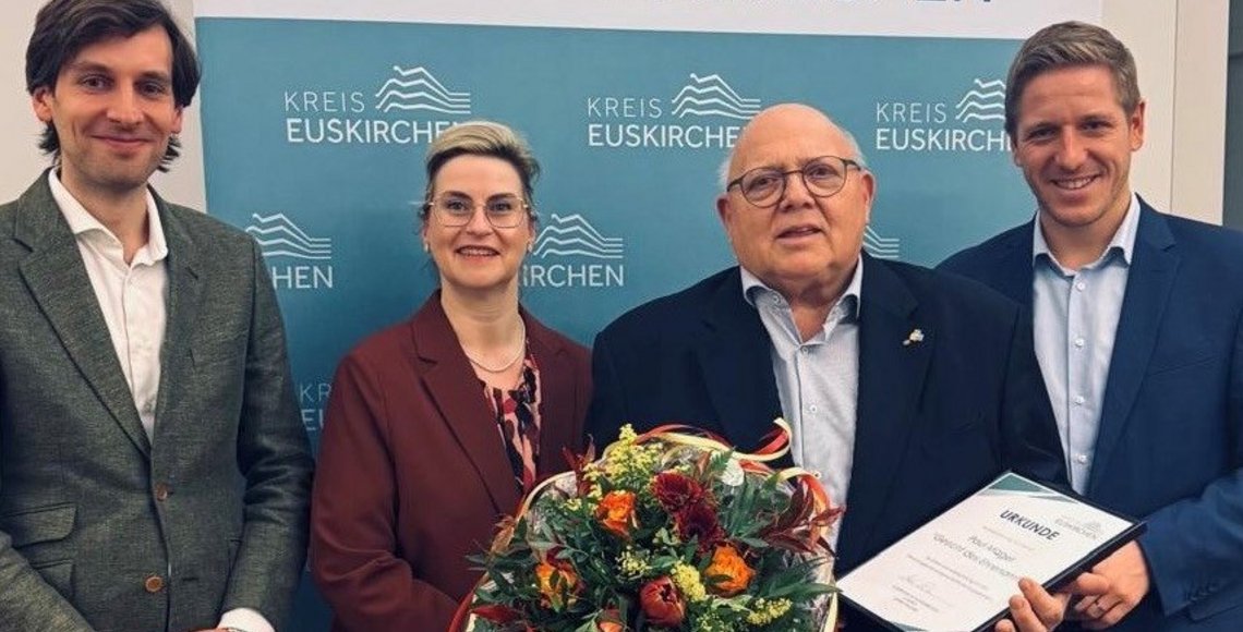 Auf dem Bild sieht man vier Personen; der zweite von rechts hält einen Blumenstrauß in der Hand"