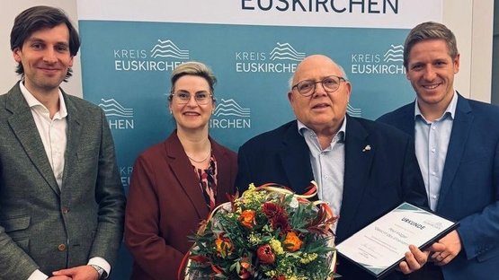 Auf dem Bild sieht man vier Personen; der zweite von rechts hält einen Blumenstrauß in der Hand"