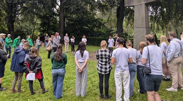 Auf dem Bild sieht man ungefähr 30 vor allem junge Menschen im Halbkreis vor einem überlebensgroßem Steinkreuz stehen.
